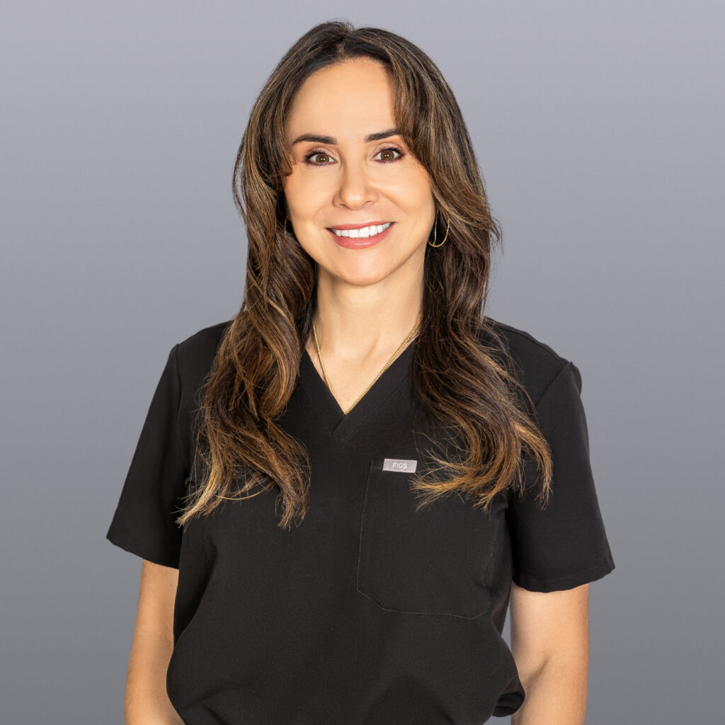Smiling woman in black scrubs with FIGS logo on the pocket, gray background.