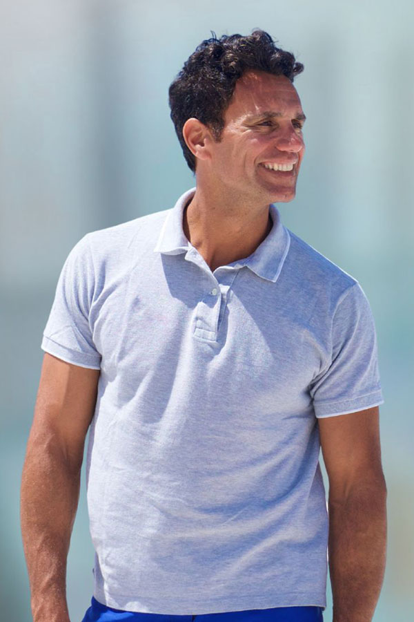 Smiling man in a light gray polo shirt outdoors, looking to his right.