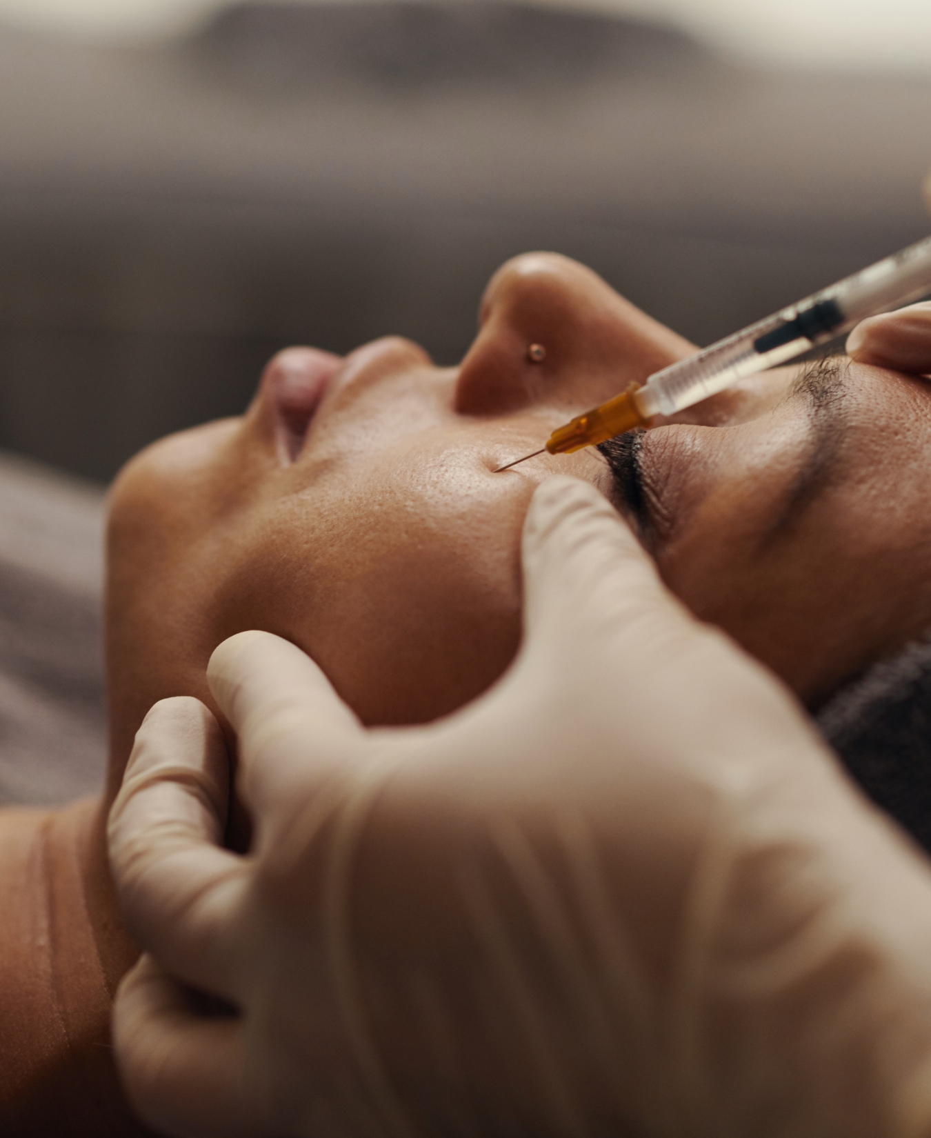 Close-up of a healthcare professional injecting a syringe near a patient’s cheek, gloved hands steadying the area.
