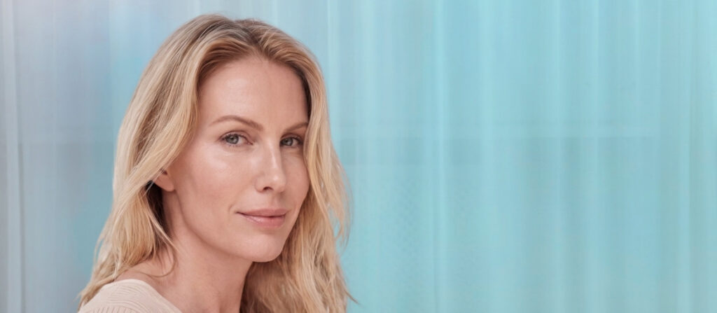 Close-up portrait of a smiling blonde woman against a light blue background.